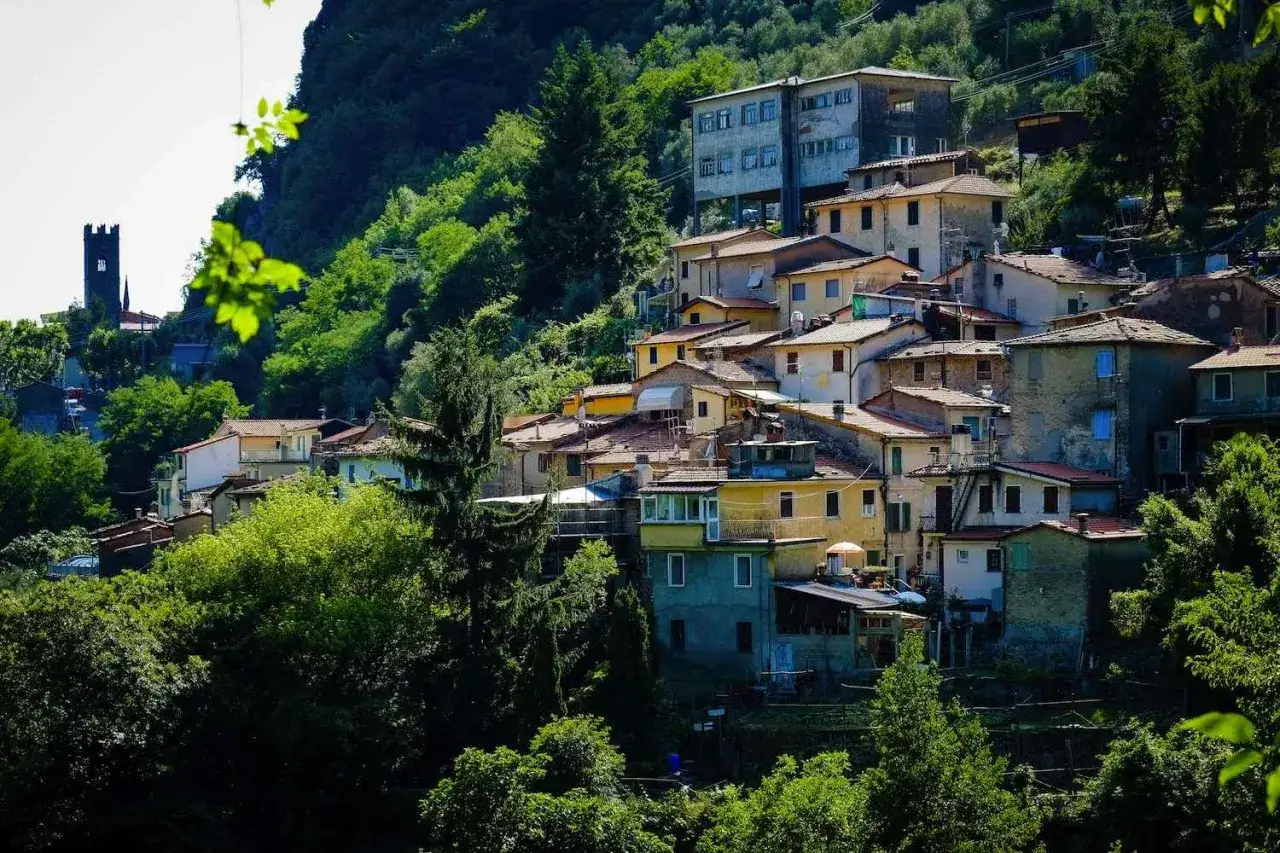 Case colorate e tetti rossi si aggrappano alla collina a Casoli di Camaiore, circondate da un verde lussureggiante.
