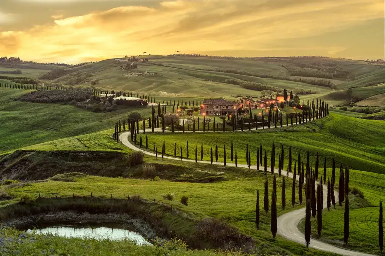 Un sogno di una settimana in Toscana: dolci colline verdi, cipressi slanciati e un casale illuminato al tramonto.