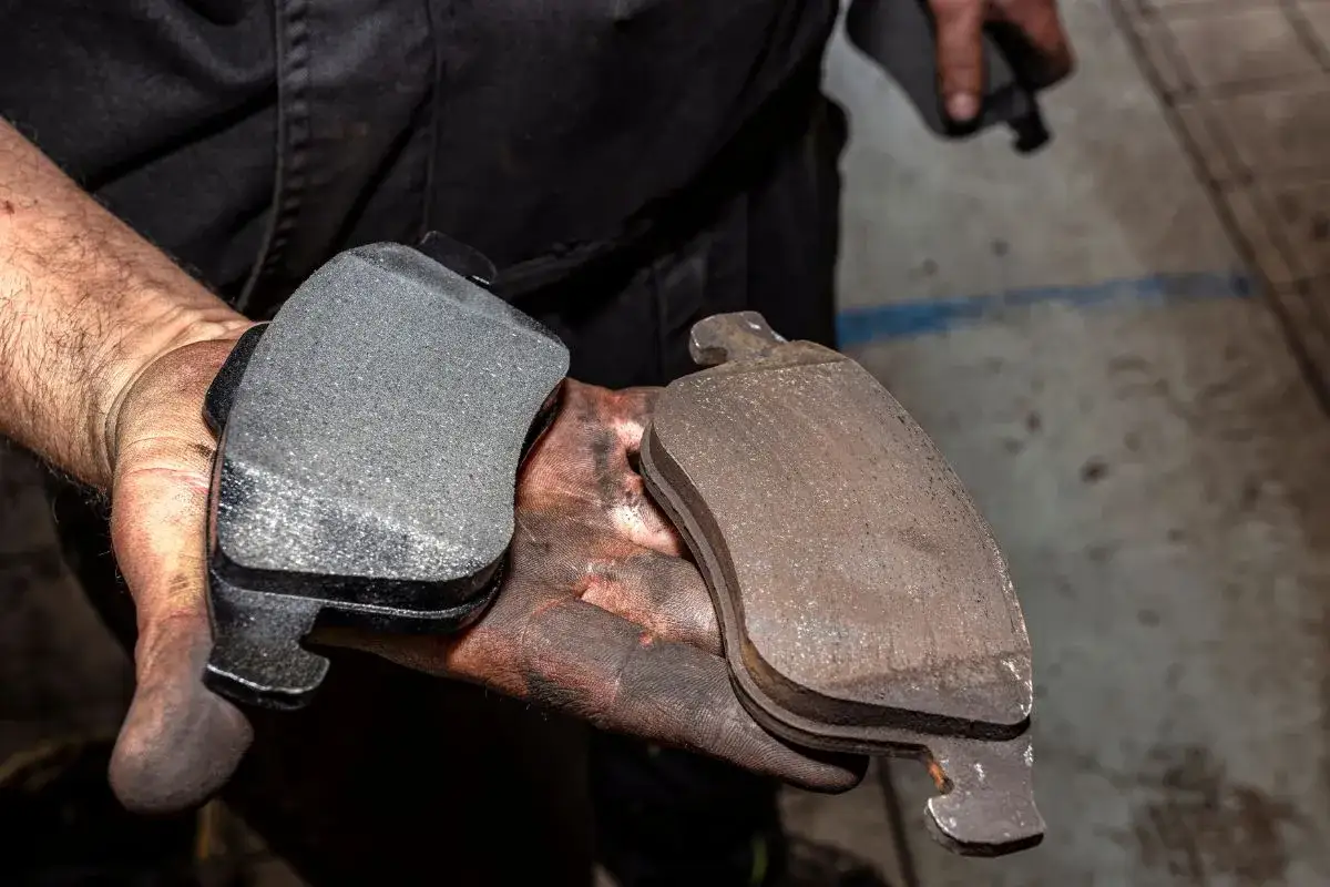Mani sporche di grasso tengono due pastiglie freni: una nuova e una consumata, che necessita di sostituzione per garantire la sicurezza.