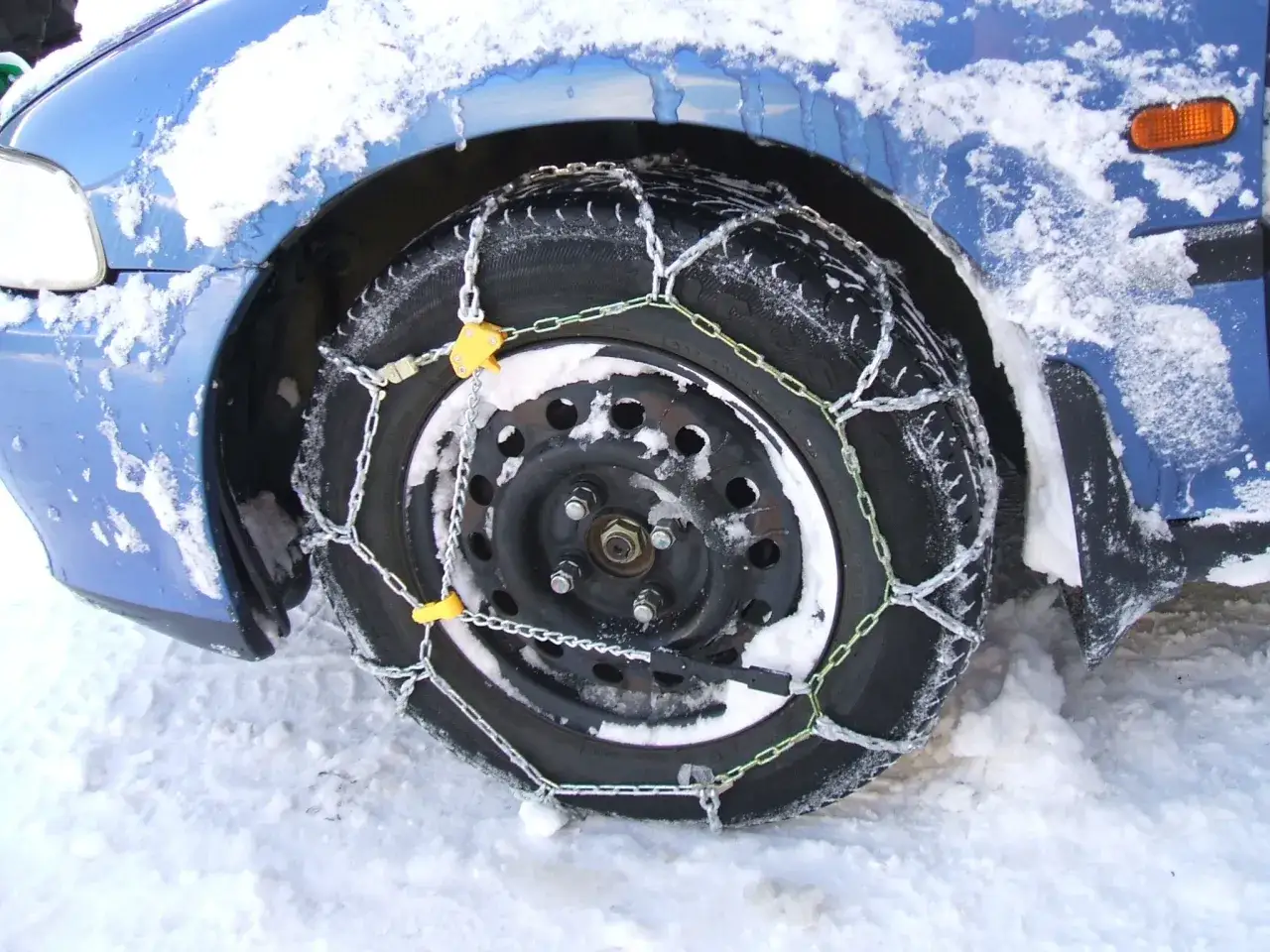 Ruota motrice di un'auto blu coperta di neve, con catene montate per affrontare il ghiaccio.