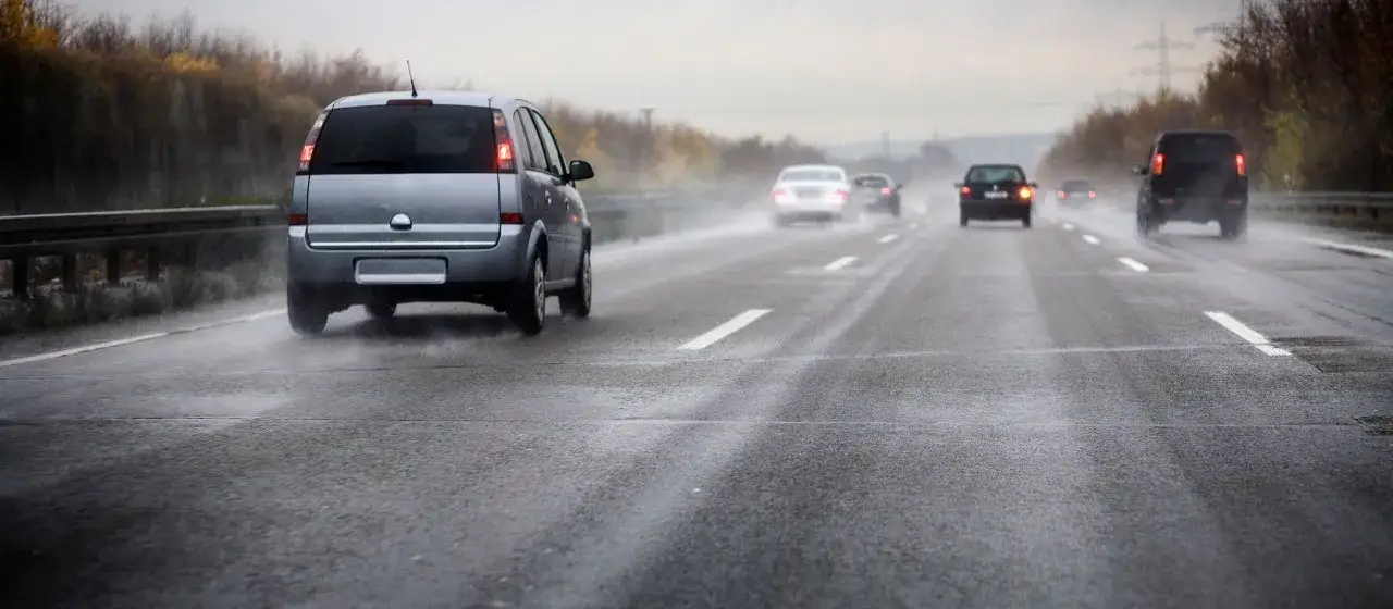 Auto su autostrada bagnata, con schizzi d'acqua che indicano il fenomeno aquaplaning. Traffico intenso in condizioni avverse.
