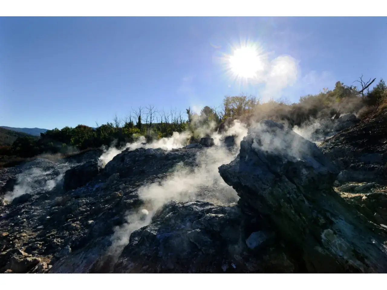 Vapori emergono da rocce vulcaniche in Toscana, ricordando i soffioni boraciferi. Il sole splende su questo paesaggio geotermico.