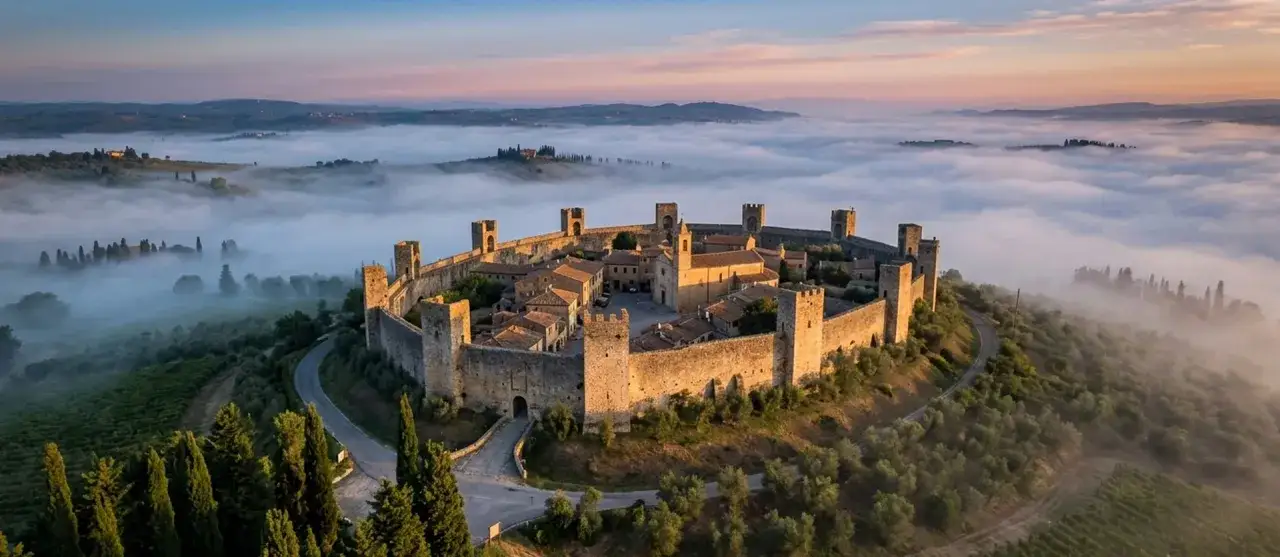 Borghi medievali vicino a Viareggio: un castello fortificato su una collina avvolta dalla nebbia all'alba, con uliveti e cipressi.