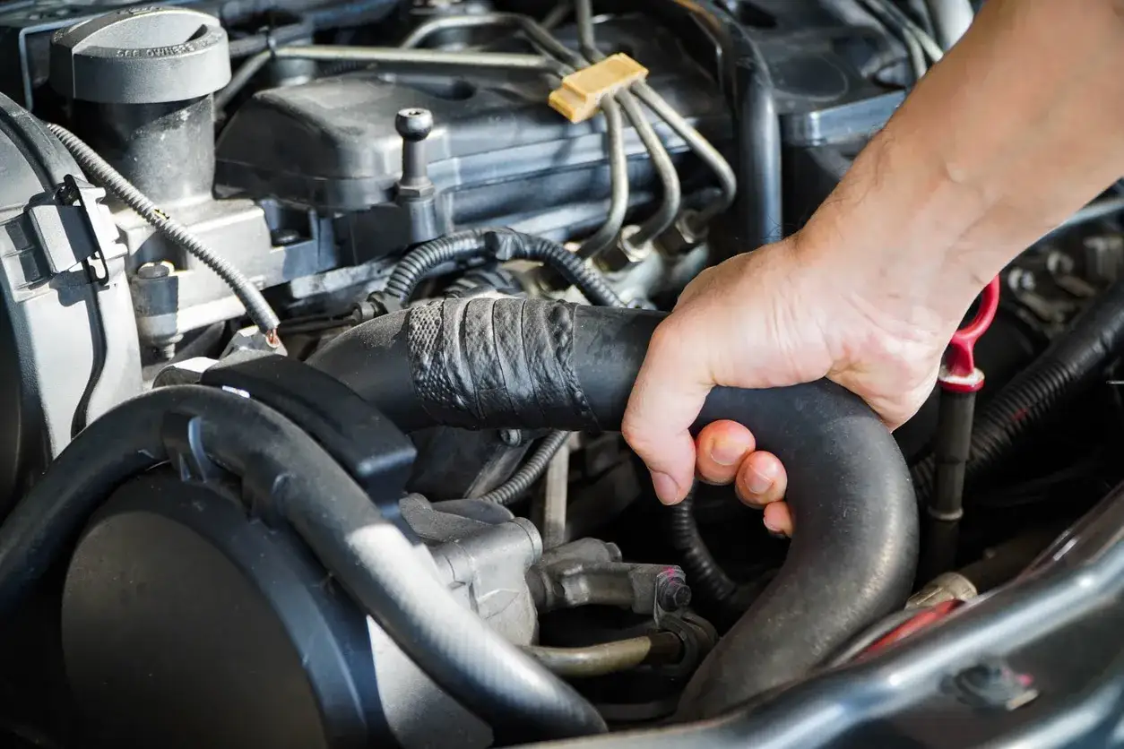 Mano che controlla un manicotto radiatore rotto, uno dei sintomi di problemi al sistema di raffreddamento.