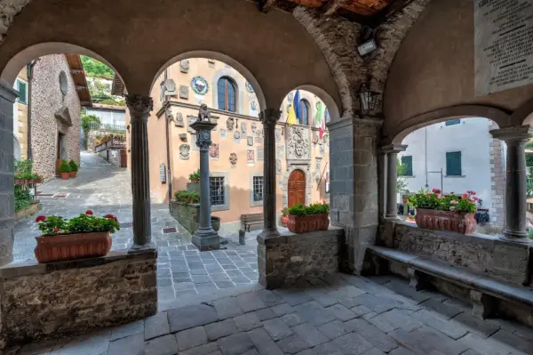 Un vicolo tra i borghi della montagna pistoiese, con archi in pietra, colonne e vasi di fiori rossi.