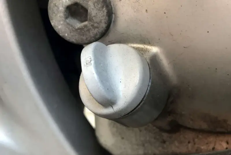 Dettaglio di un tappo motore con una piccola crepa, suggerendo una possibile fuoriuscita olio motore dal tappo.