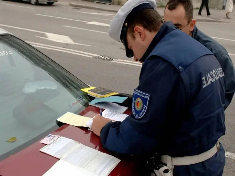 Agente di polizia scrive verbale su un'auto con revisione scaduta da 2 anni. Documenti e patente sul cofano.